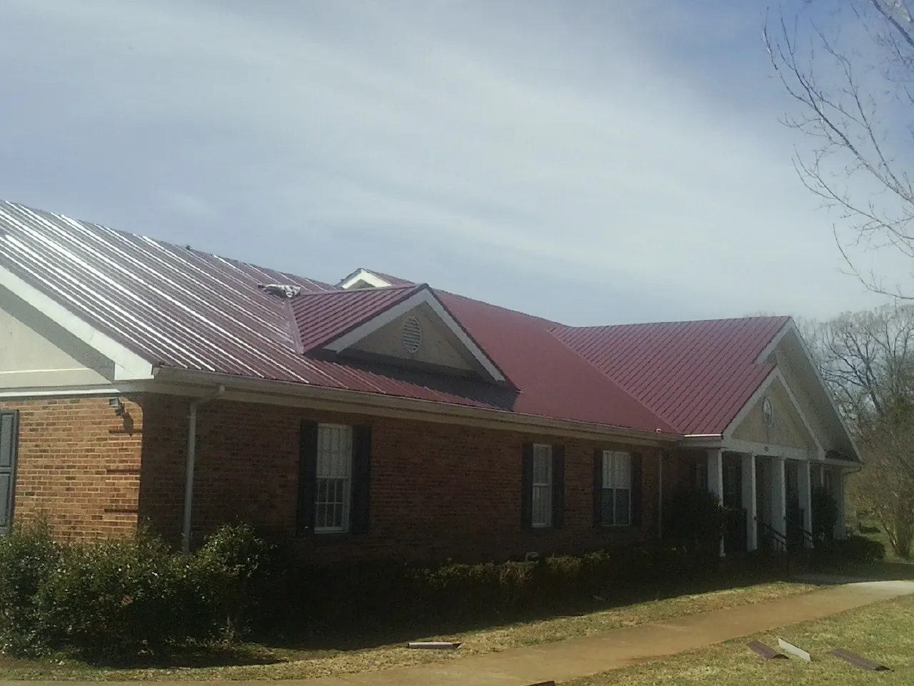 Red metal roof with gabled entries on a long brick building, from a Hail Damage Roof Repair job in Potsdam