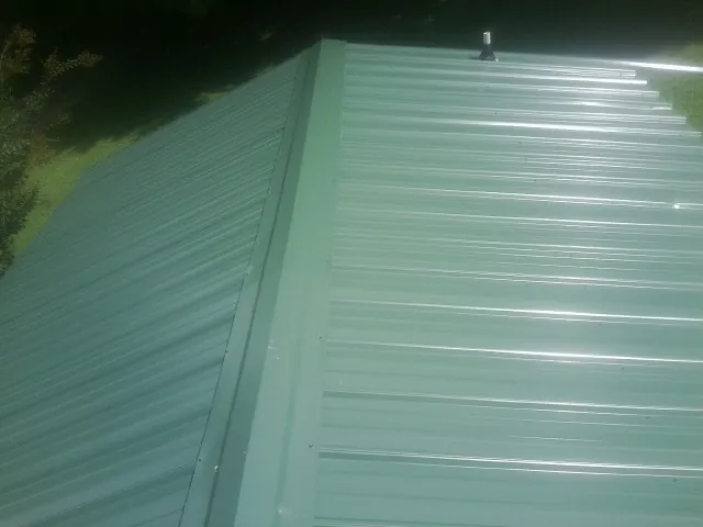New green metal panels meeting at the ridge of a roof — Flat Roof Repair work by our crew in Potsdam