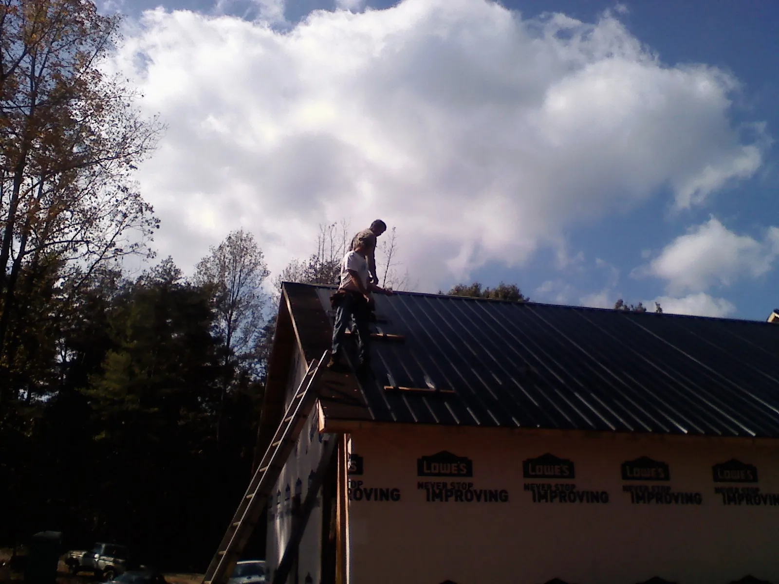 Roofer fastening dark metal panels high against a cloudy sky, from a Roof Inspection job in Potsdam