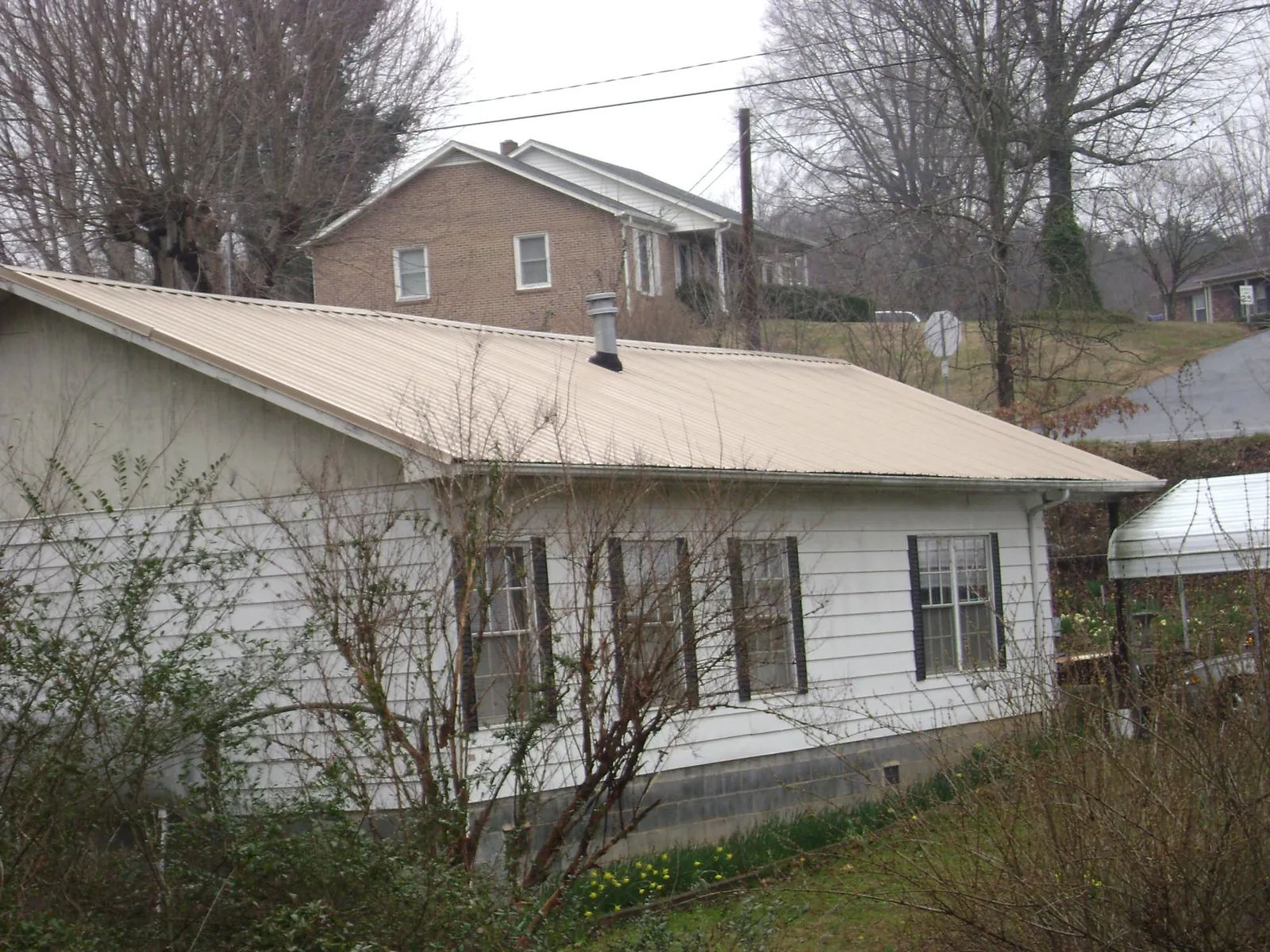 Tan metal roof on a white sided house set into a hillside — Commercial Roofing by Roofing Brothers in Potsdam