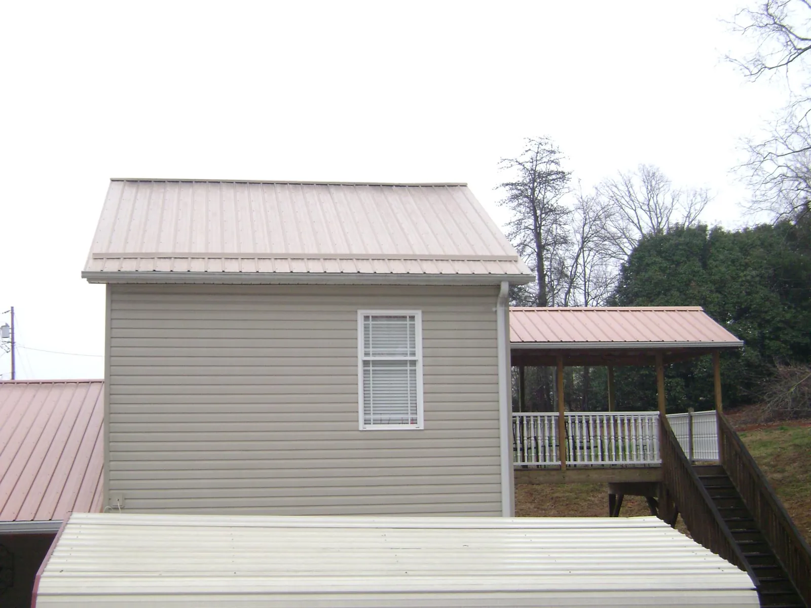 Tan metal roofs on a two story addition and attached porch, from a Roof Replacement job in Potsdam